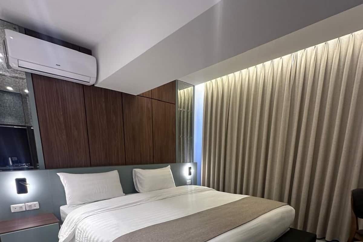 A modern bedroom with a large bed, built-in headboard, bedside tables, and an air conditioning unit.