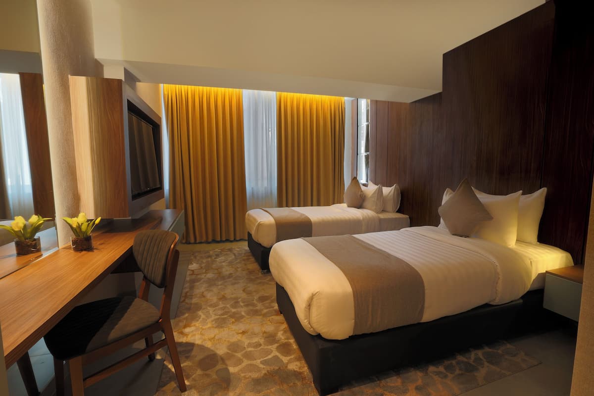 A hotel room with two beds, a desk, a chair, and a TV.