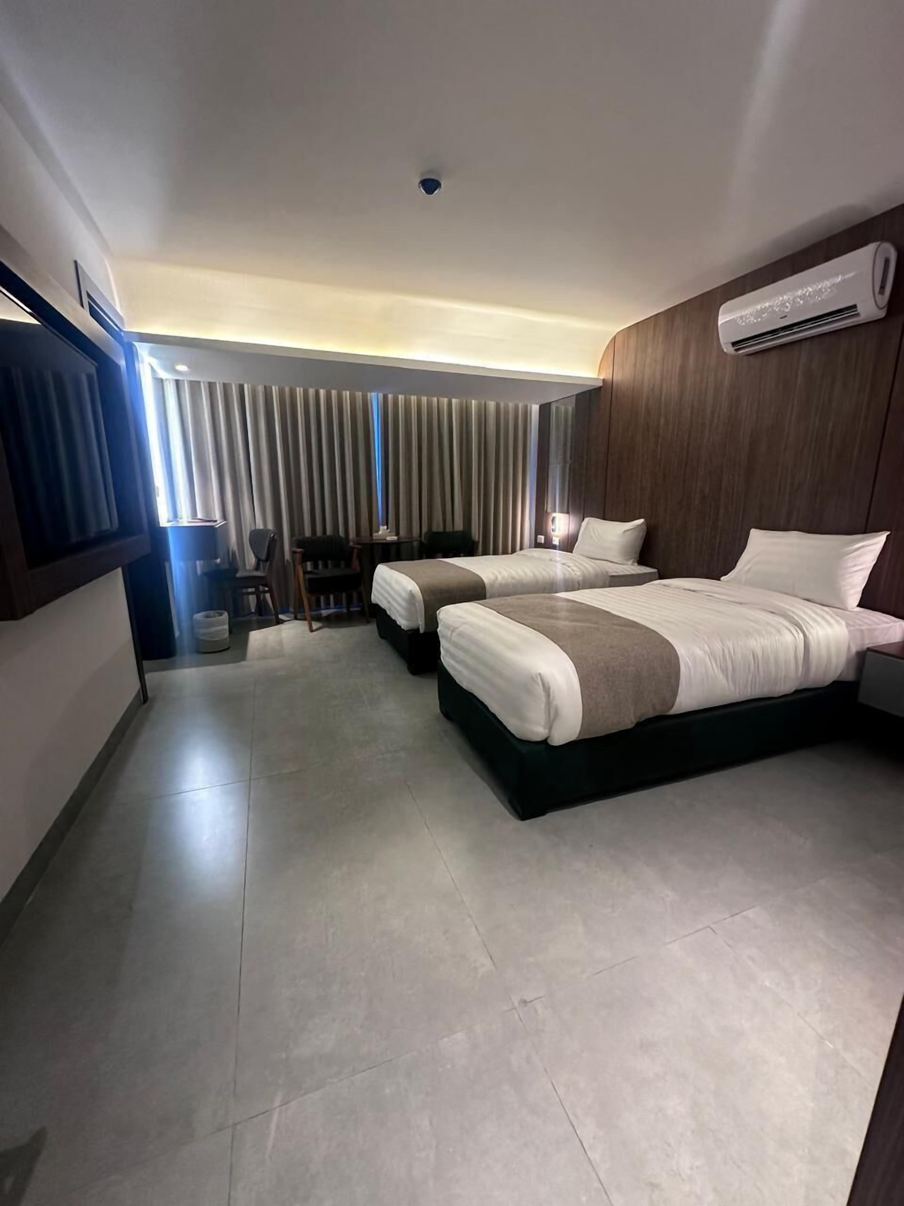 A hotel room with two beds, a TV, a desk, and a window with curtains.