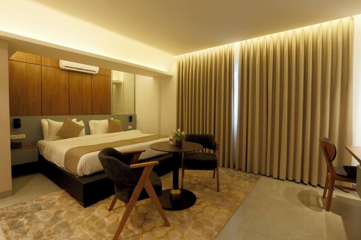 A hotel room with a bed, a small table, a chair, a desk, a mirror, and a window with curtains.