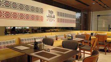 A modern restaurant with a central seating area, a bar, and a mirrored wall.