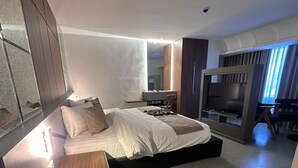 Un dormitorio moderno con una cama grande, un banco de madera, un escritorio y un televisor.
