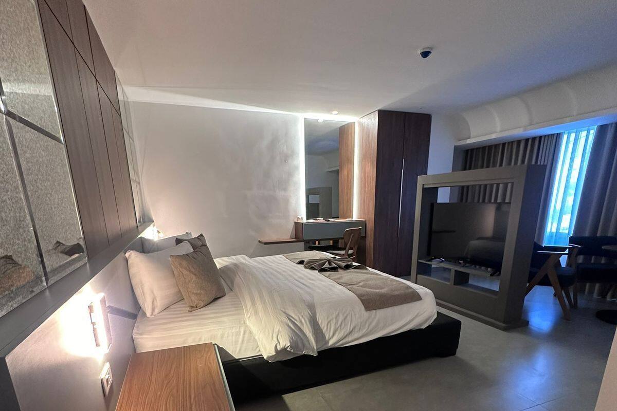 A modern bedroom with a large bed, a wooden bench, a desk, and a TV.