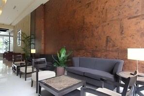 A lobby with a grey sofa, chairs, a coffee table, and a potted plant. - B Hotel Alabang (Muntinlupa)