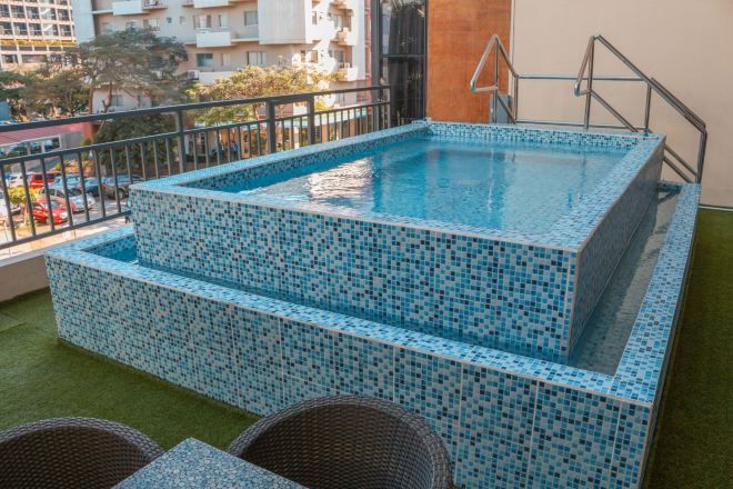 A small outdoor swimming pool with mosaic tiles, surrounded by a metal railing and wicker chairs.