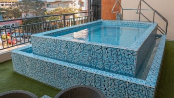 A small outdoor swimming pool with mosaic tiles, surrounded by a metal railing and wicker chairs.