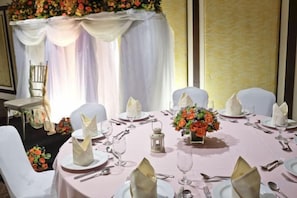 A round table set for six with white chairs, a vase of flowers, and a small table lamp. - B Hotel Alabang (Muntinlupa)