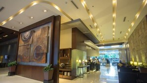 A modern hotel lobby with a large abstract painting, a reception desk, and seating areas. - B Hotel Alabang (Muntinlupa)