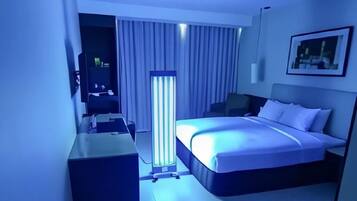A hotel room with a bed, a desk, a chair, a TV, and a standing lamp.