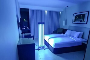 A hotel room with a bed, a desk, a chair, a TV, and a standing lamp. - B Hotel Alabang (Muntinlupa)