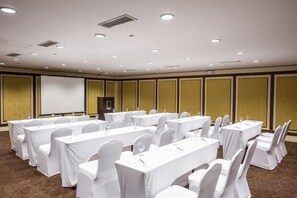 Un salón de conferencias con varias mesas y sillas, una pantalla de proyector y un atril.