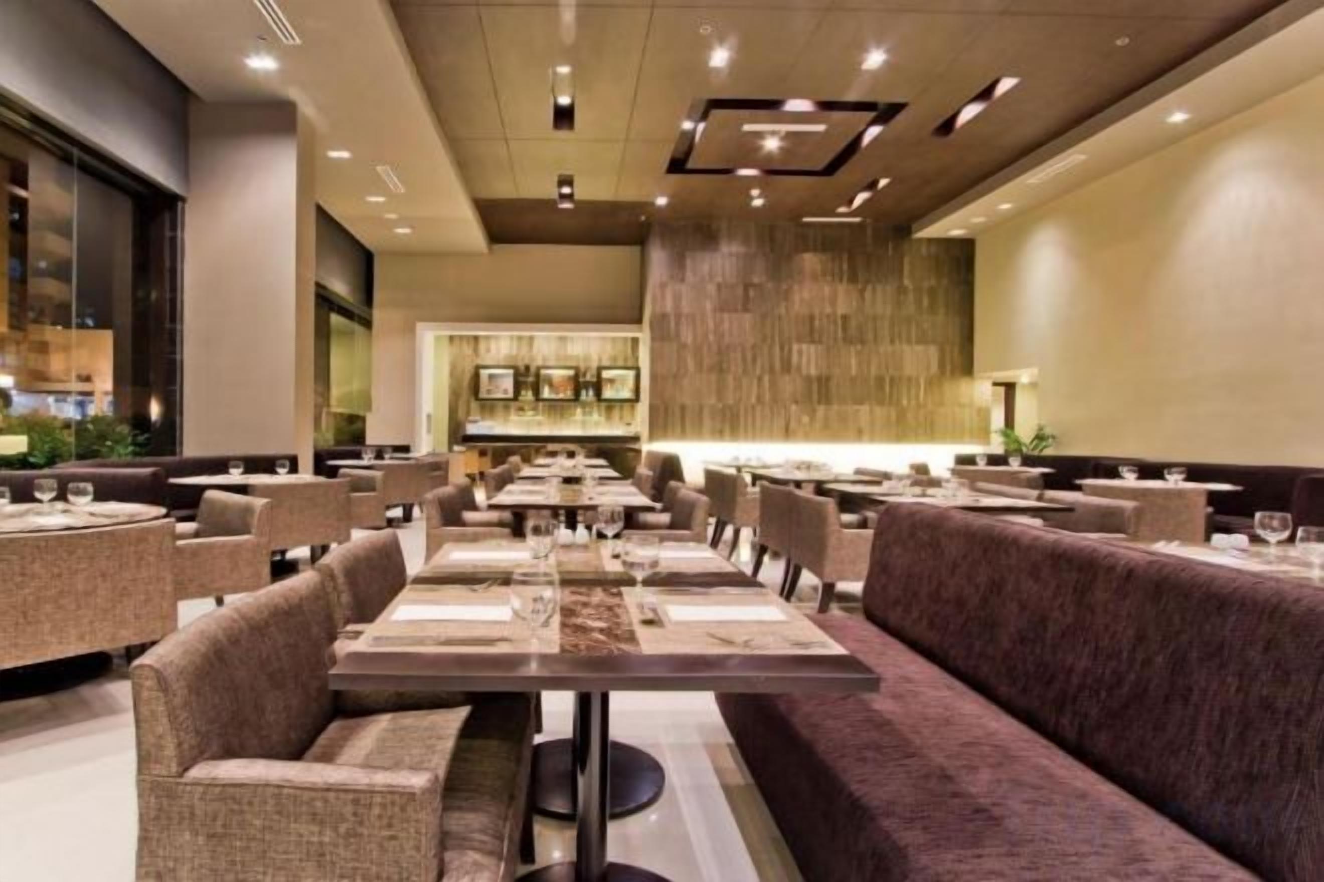 Un restaurante moderno con varias mesas y cabinas, una zona de bar y un techo alto con iluminación empotrada.