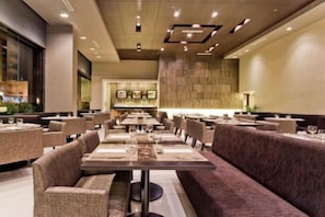 En modern restaurang med flera bord och avskilda sittgrupper, en bardisk och ett högt tak med infälld belysning.