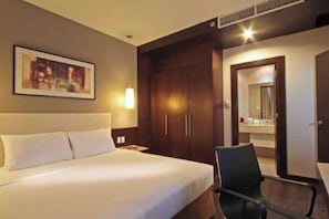 Ett hotellrum med en säng, en stol, en garderob och en spegel.