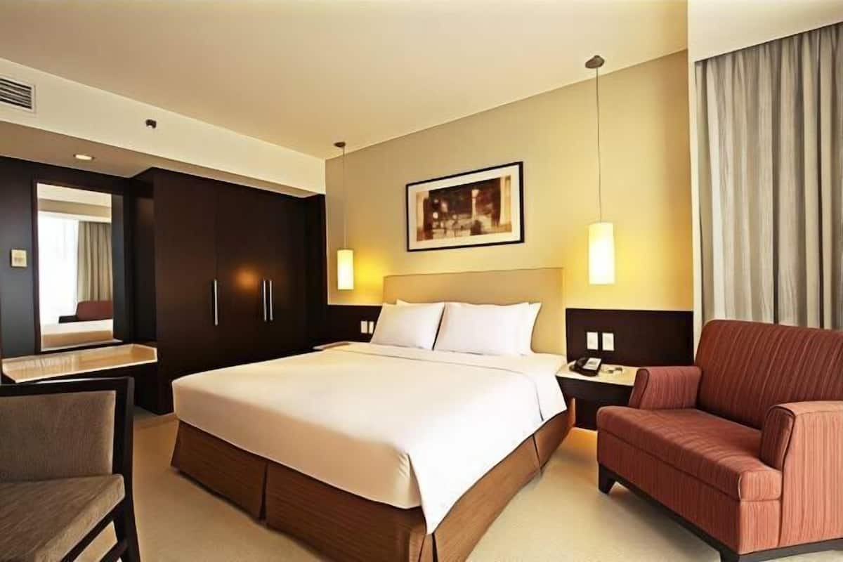 Ein Hotelzimmer mit einem großen Bett, einem Schreibtisch, einem Sessel, einem Nachttisch und einer Wandleuchte.
