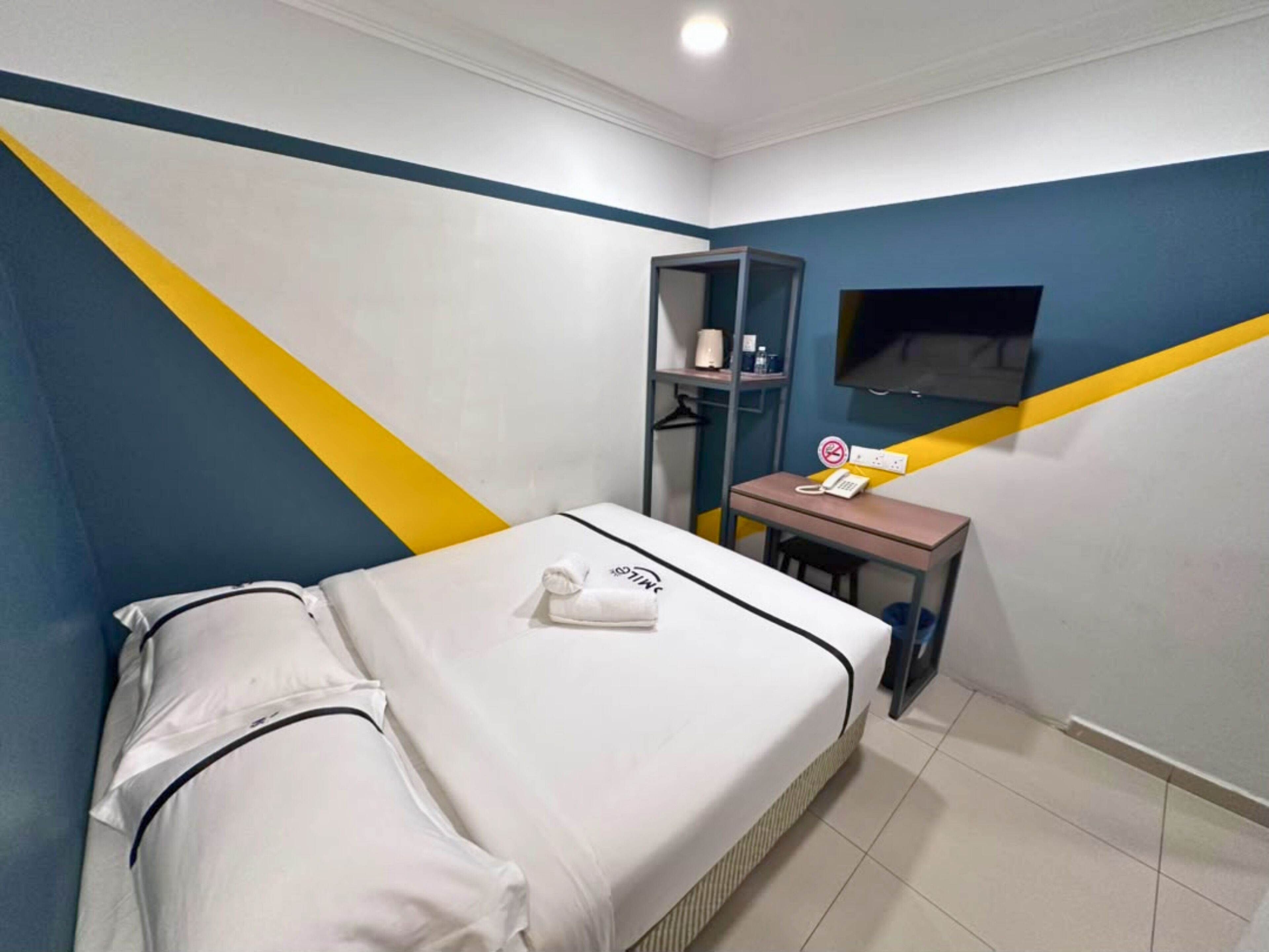 A bedroom with a bed, a desk, a chair, a TV, and a shelf with toiletries.
