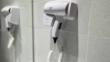 Um secador de cabelo fixado numa parede revestida de azulejos, provavelmente em uma casa de banho ou ambiente semelhante.