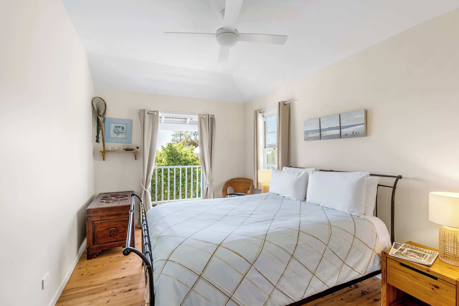 Ein Schlafzimmer mit Bett, Deckenventilator, Nachttisch aus Holz, Korbsessel und Blick ins Grüne.