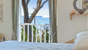 Un dormitorio con vista al mar a través de una puerta de balcón, una cama y una mesita de noche.