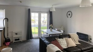 Una sala de estar moderna con un sofá de cuero negro, una mesa de comedor y un ventanal con cortinas.