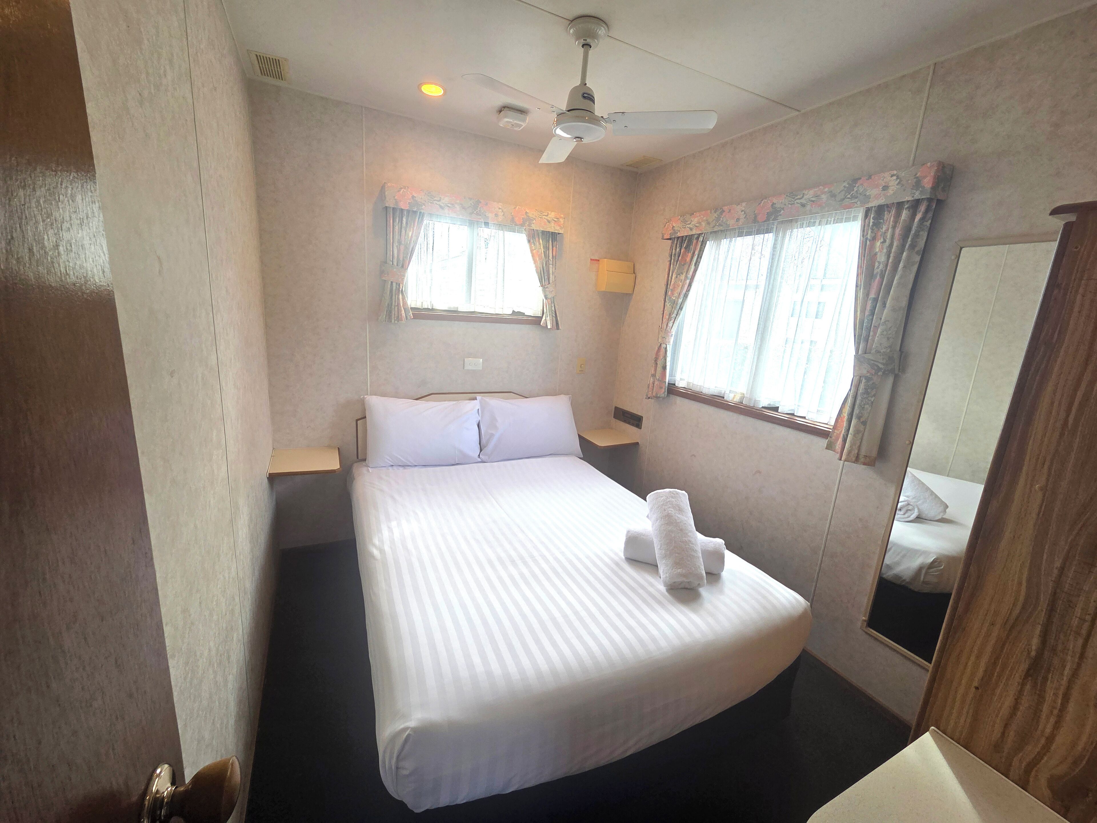 A hotel room with a large bed, a ceiling fan, and two windows with curtains.