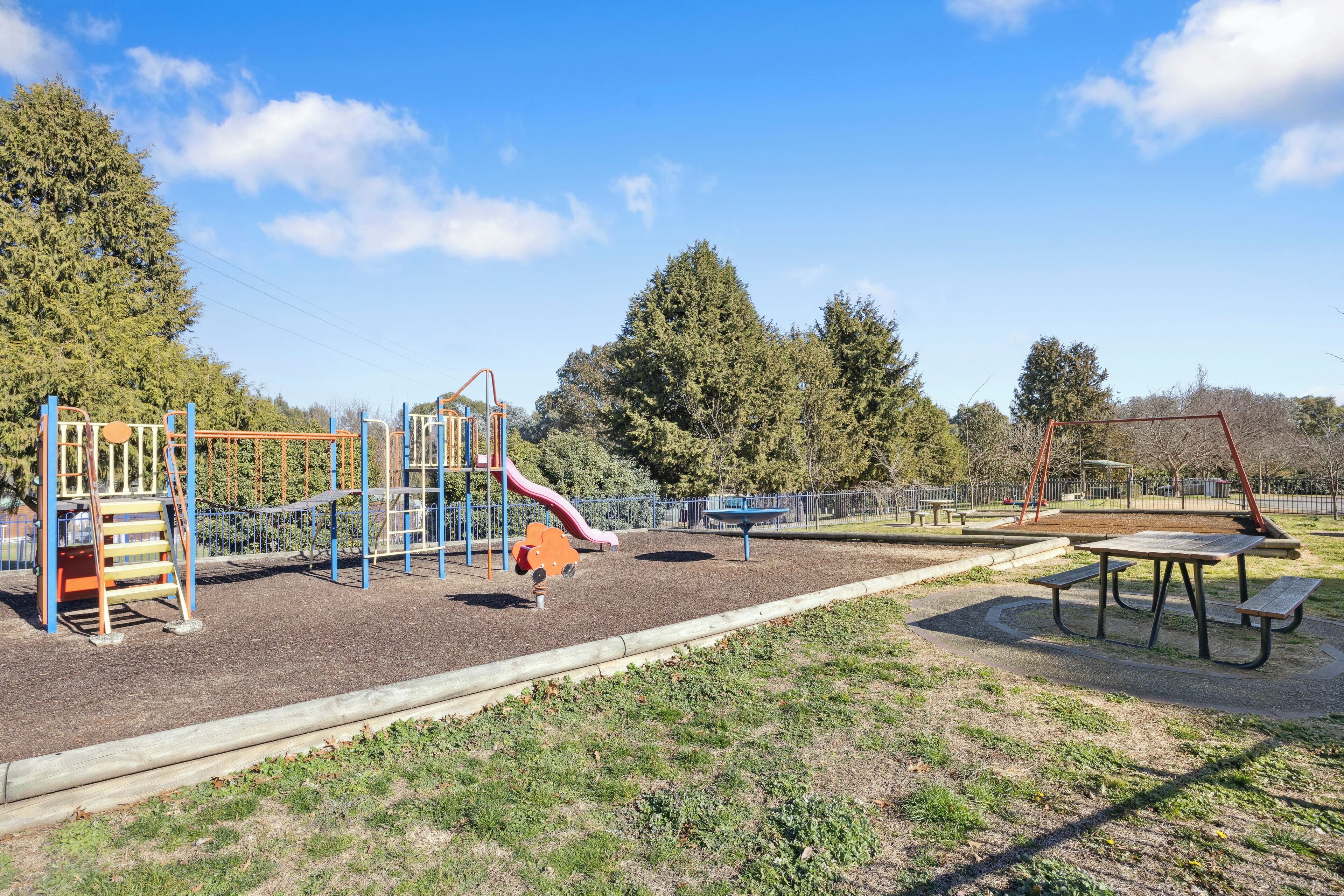 Un parque infantil con un tobogán, estructuras para escalar y una mesa de picnic.