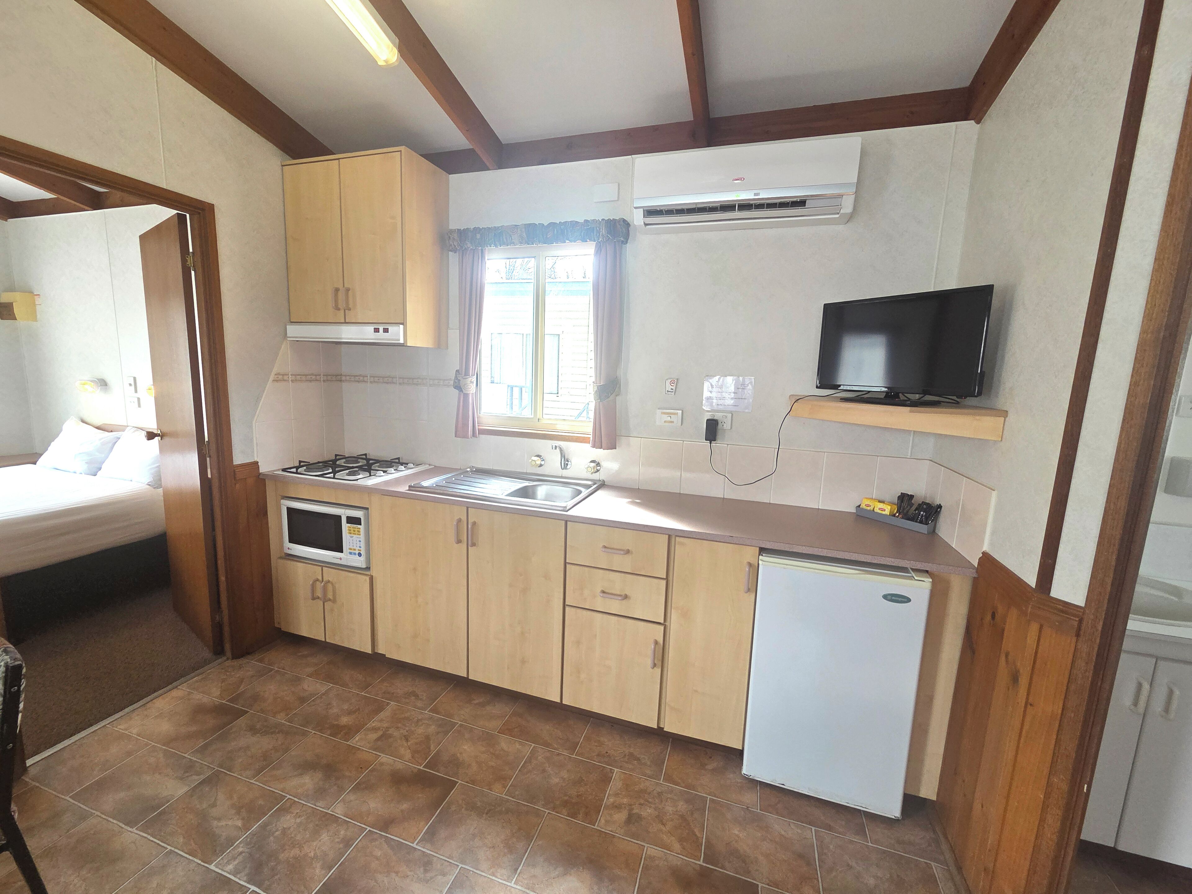 A compact kitchen with wooden cabinets, a microwave, a gas stove, a sink, and a small refrigerator.