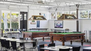 A billiards hall with two pool tables, chairs, and a billiard cue rack.
