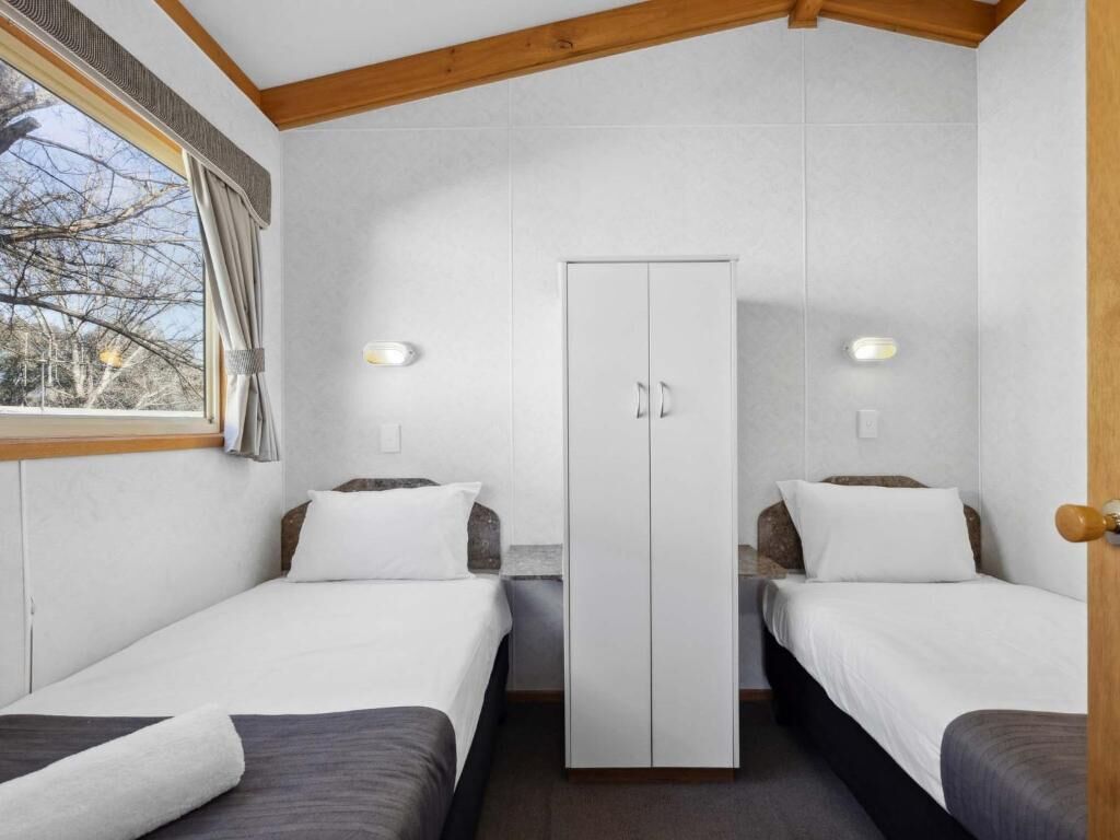 A room with two beds, a wardrobe, and a window with curtains.