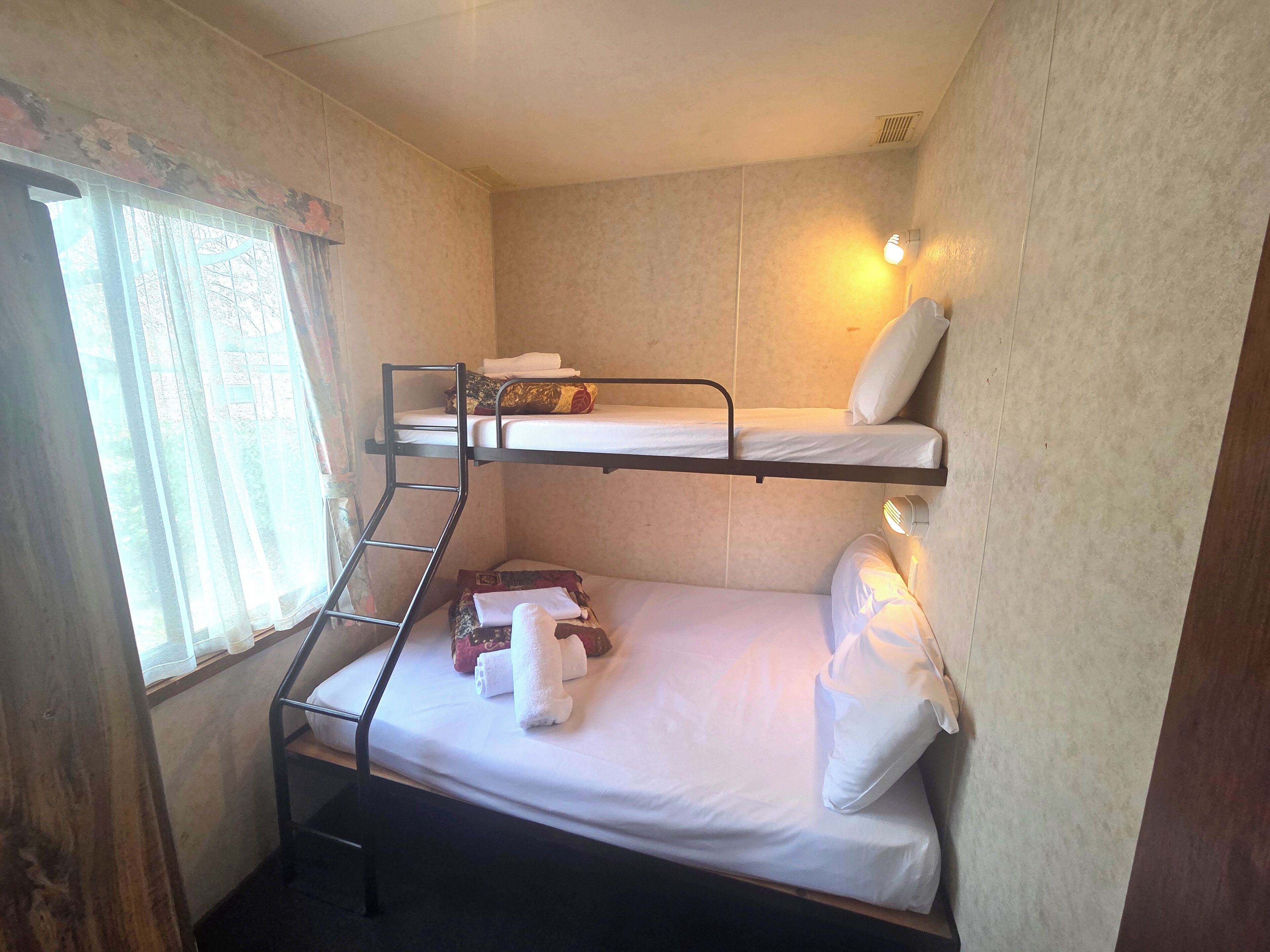 A bunk bed room with a ladder, a window with curtains, and a wall-mounted light.
