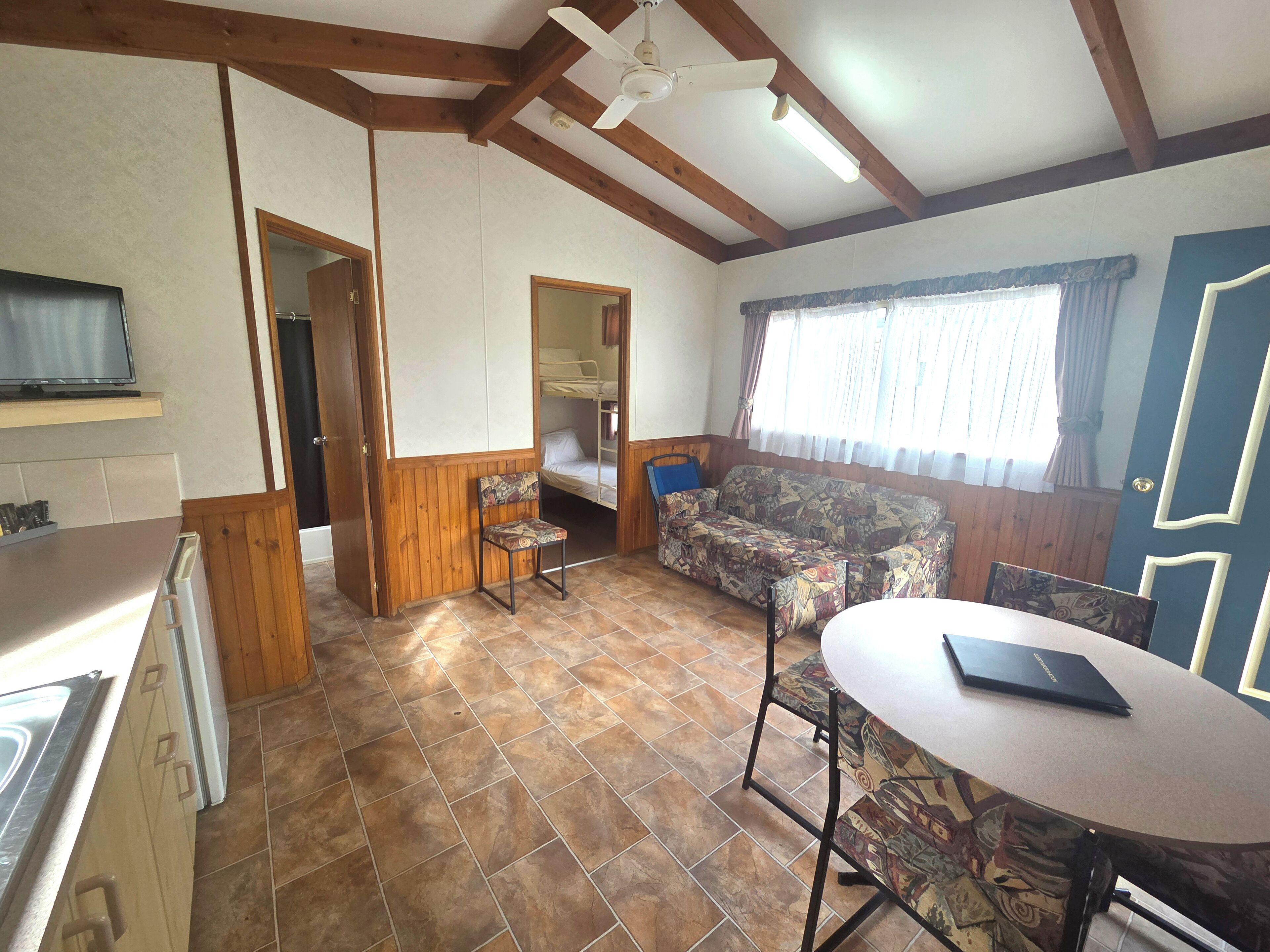 Una habitación compacta con kitchenette, un sofá, una mesa de comedor y un ventilador de techo.