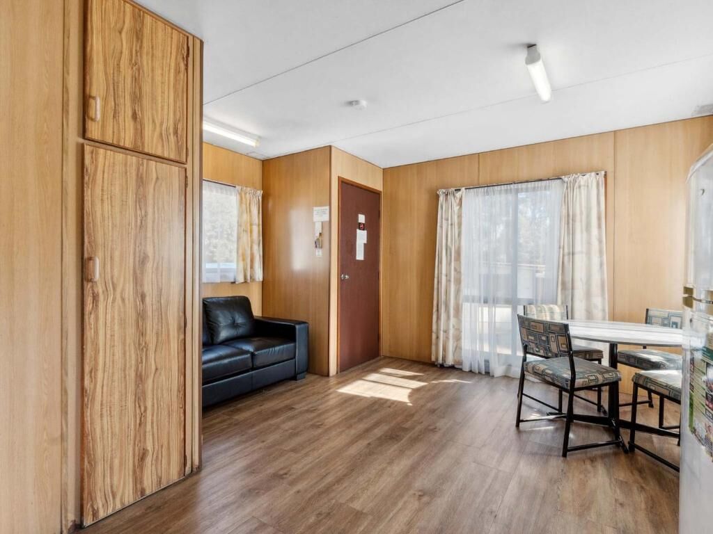 Una habitación con paneles de madera, un sofá de cuero negro, una mesa de comedor con cuatro sillas y un refrigerador.