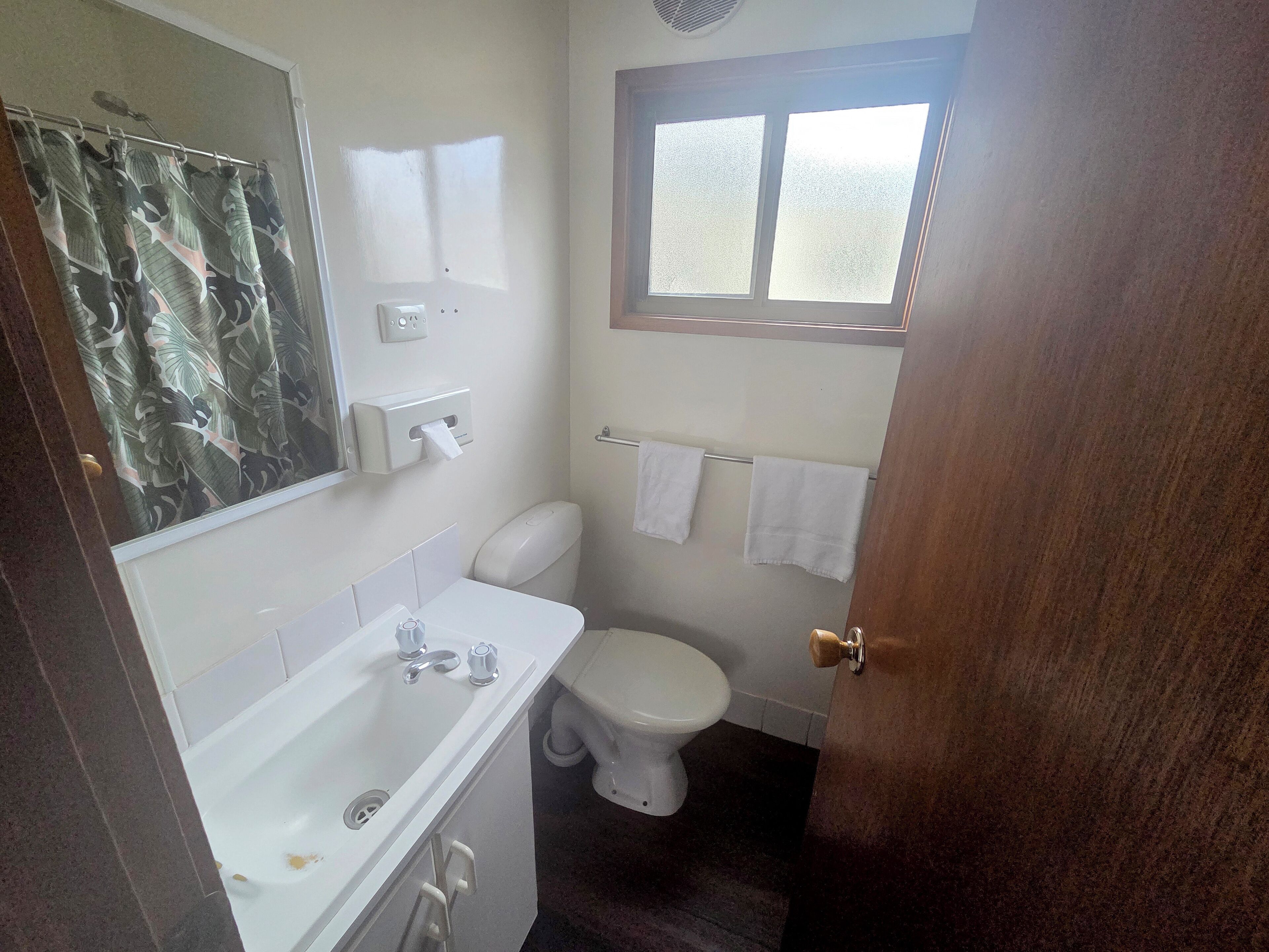 A bathroom with a toilet, sink, and a window.