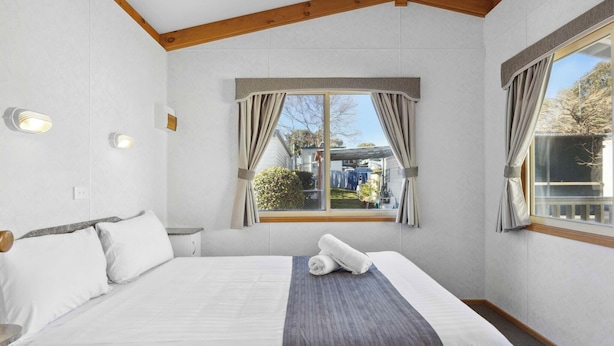 Ein Schlafzimmer mit einem Bett, einem Fenster mit Vorhängen, Blick ins Freie und einer Decke mit Holzbalken.