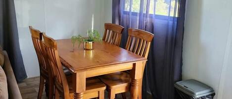 Un comedor con una mesa y sillas de madera, una planta en maceta y una ventana con cortinas.