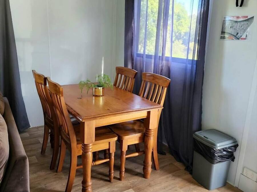 A dining area with a wooden table and chairs, a potted plant, and a window with curtains.