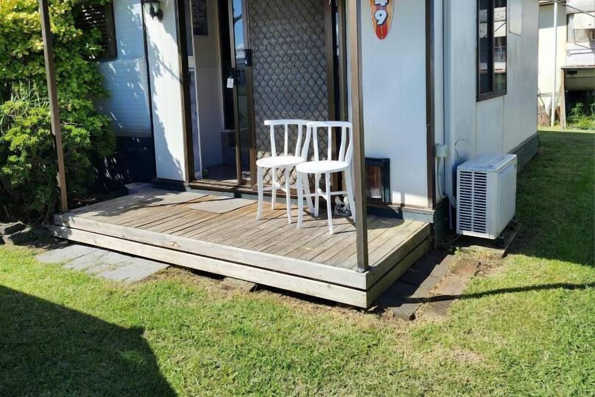 A small, single-story building with a covered patio area, a white chair, and an air conditioning unit.