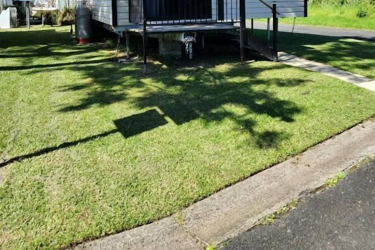 A mobile home with a porch and a small deck, surrounded by grass and trees.