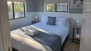 A neatly made bed with a patterned blanket, two bedside lamps, and a painting on the wall. - Shellharbour Holiday Village (Barrack Point)
