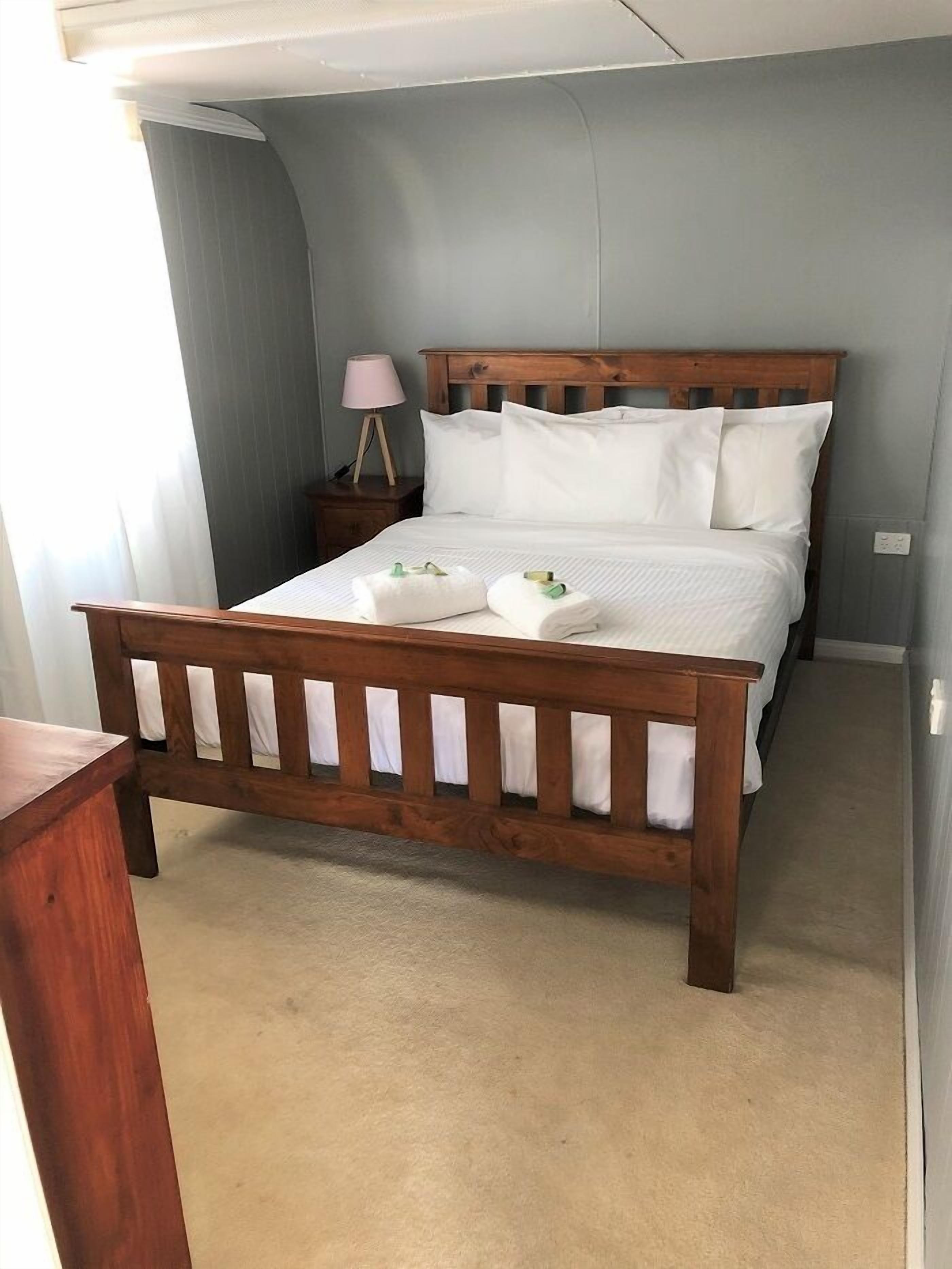 A neatly made bed with white linens and towels, a wooden headboard, and a bedside lamp on a nightstand.