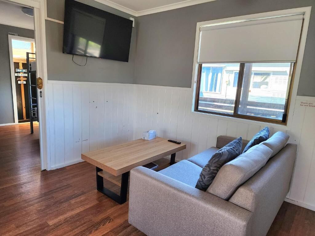 Una sala de estar con un sofá, una mesa de madera, un televisor de pantalla plana montado en la pared y una ventana con persianas.