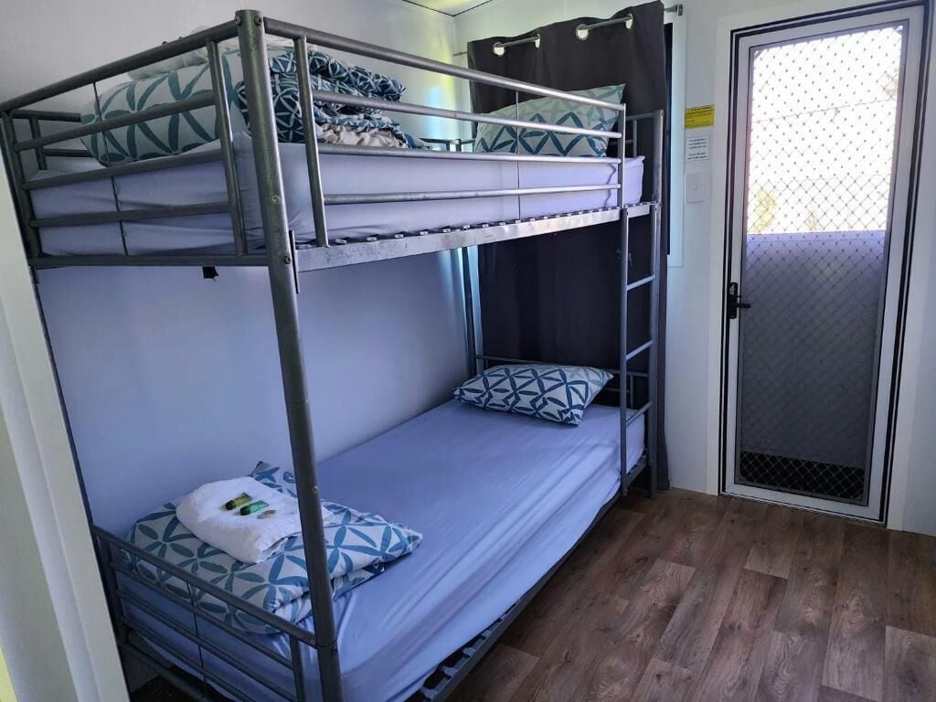 Habitación con literas de metal, una puerta con mosquitera y suelo de madera.