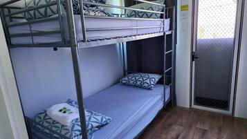 Habitación con literas de metal, una puerta con mosquitera y suelo de madera.