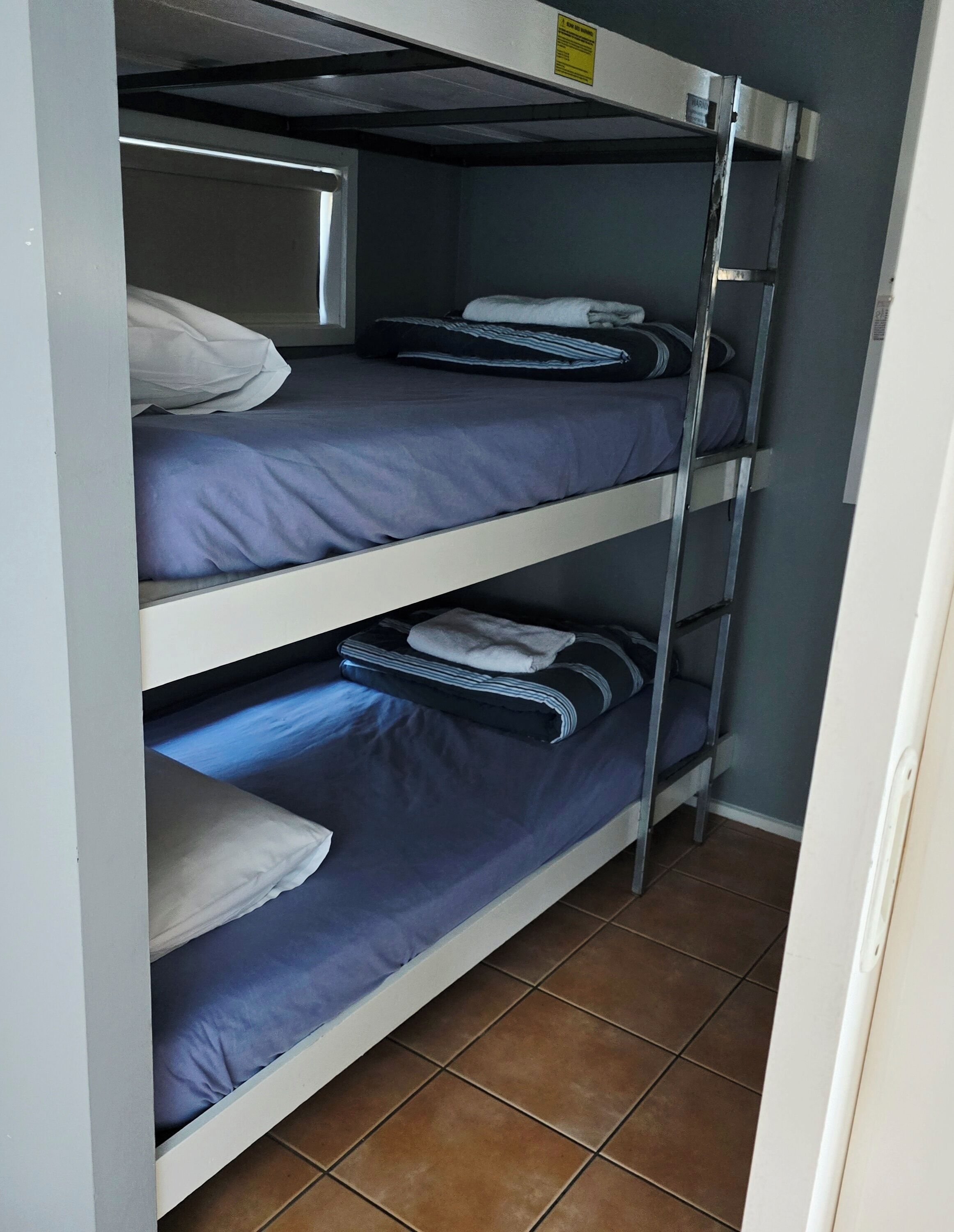 Une chambre avec des lits superposés à trois niveaux, chaque lit étant équipé d’un matelas et d’oreillers.