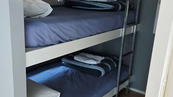 Une chambre avec des lits superposés à trois niveaux, chaque lit étant équipé d’un matelas et d’oreillers.