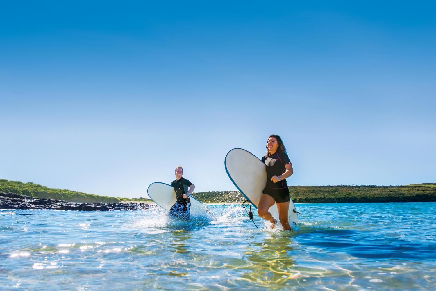 Dos personas corriendo al agua con tablas de surf.