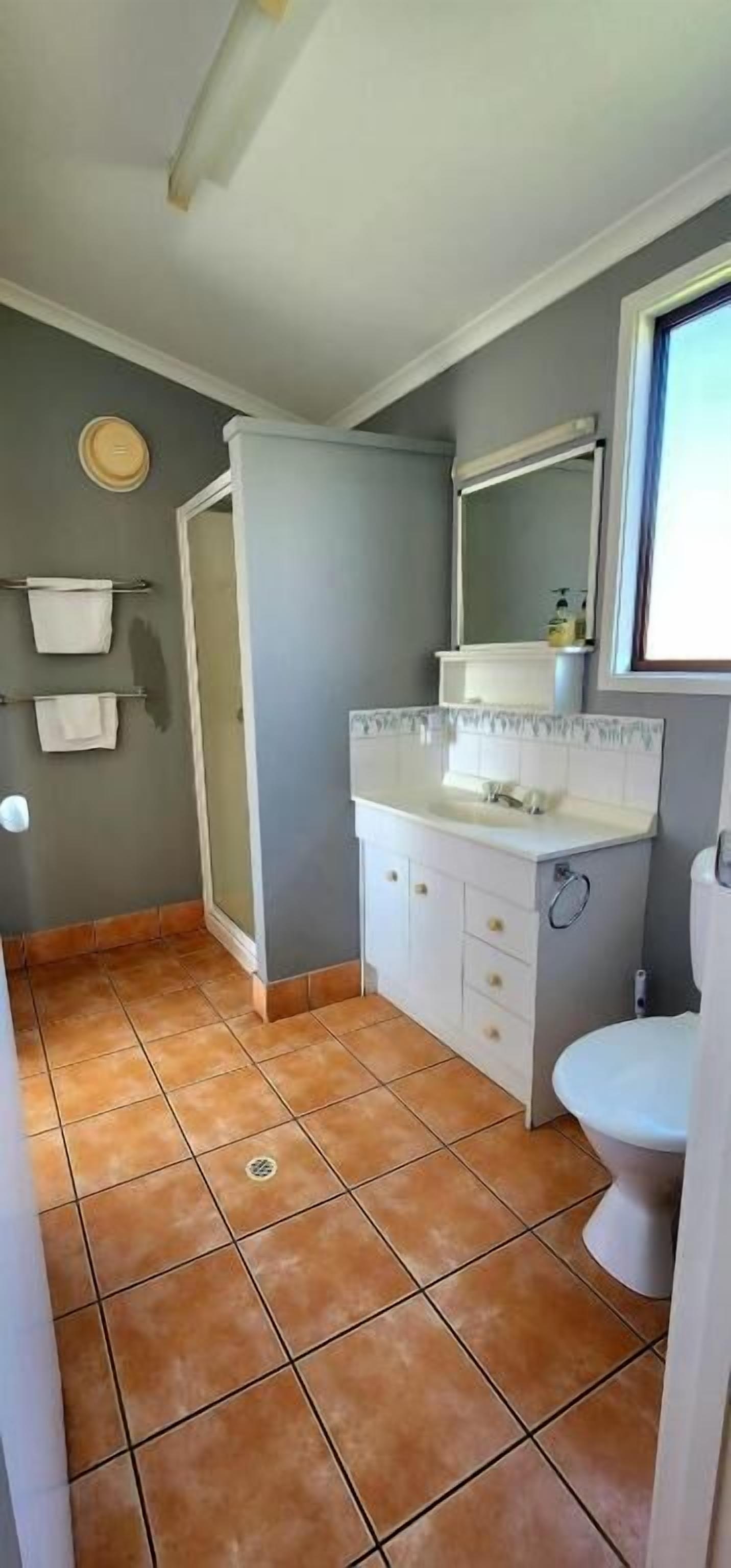 A bathroom with a white sink, mirror, and toilet. There is a towel rack with two towels and a small window above the sink.
