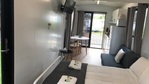 A modern hotel room with a bed, a small table, a TV, and a balcony with a table and chairs. - Shellharbour Holiday Village (Barrack Point)