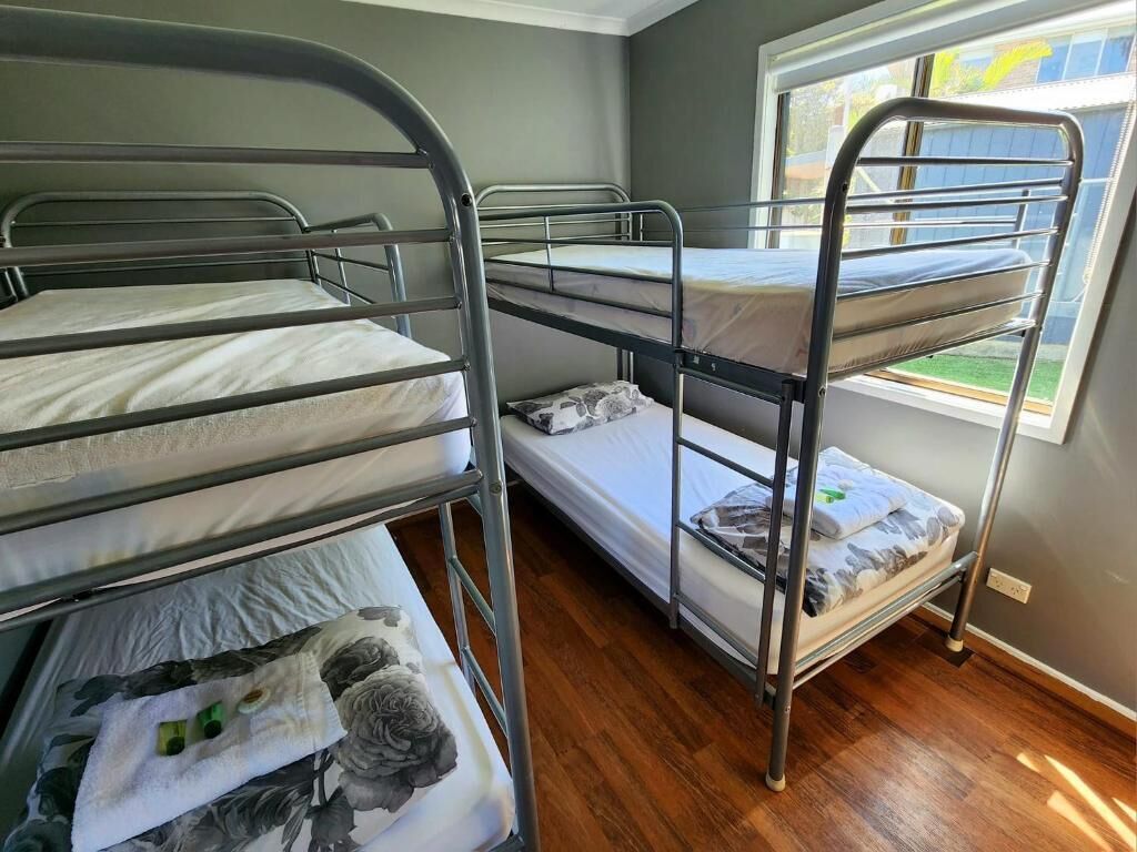A bunk bed room with three levels, a window with a view of a yard, and a wooden floor.