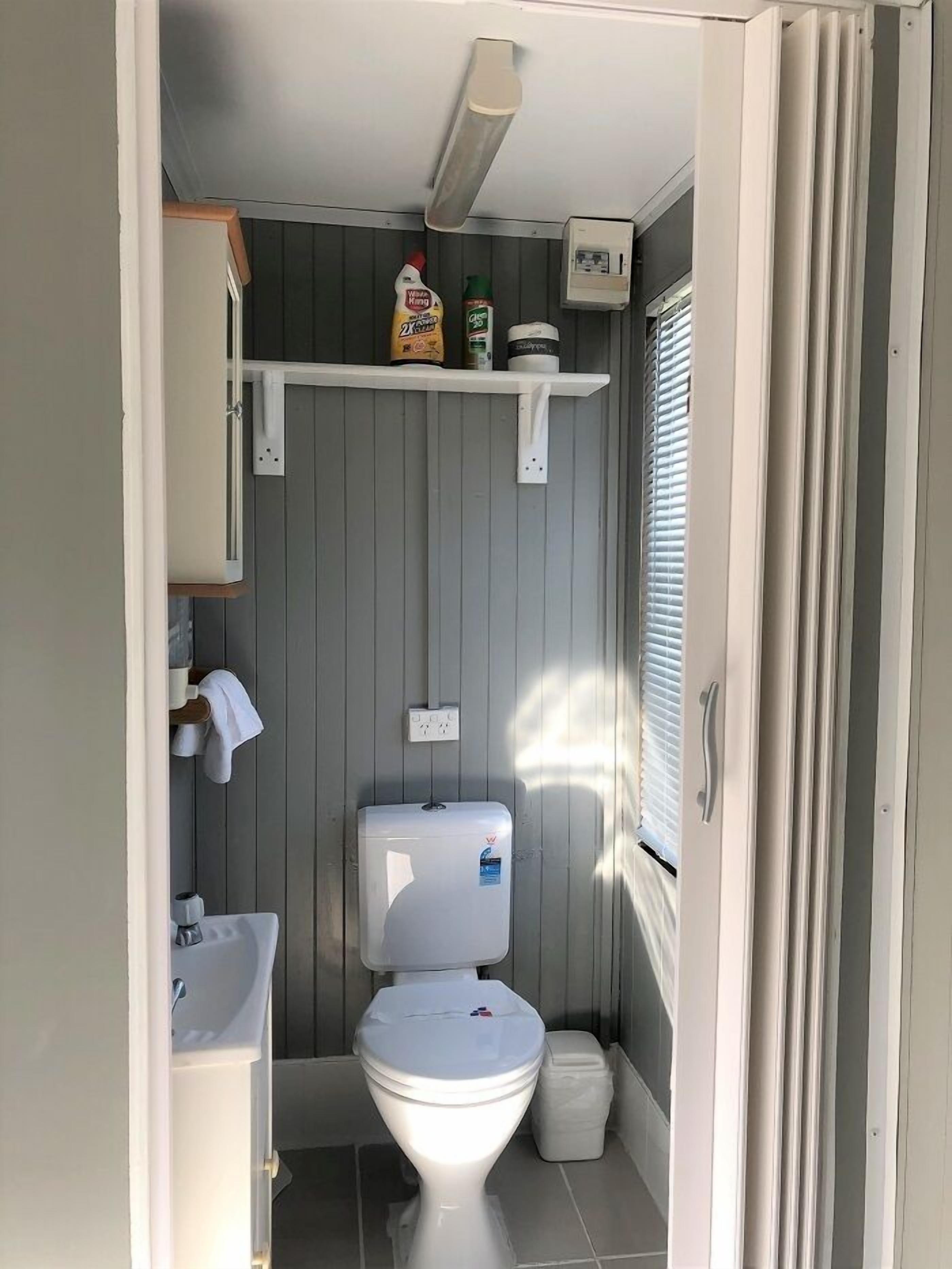 Un baño pequeño con inodoro, lavamanos y un estante con artículos de aseo.